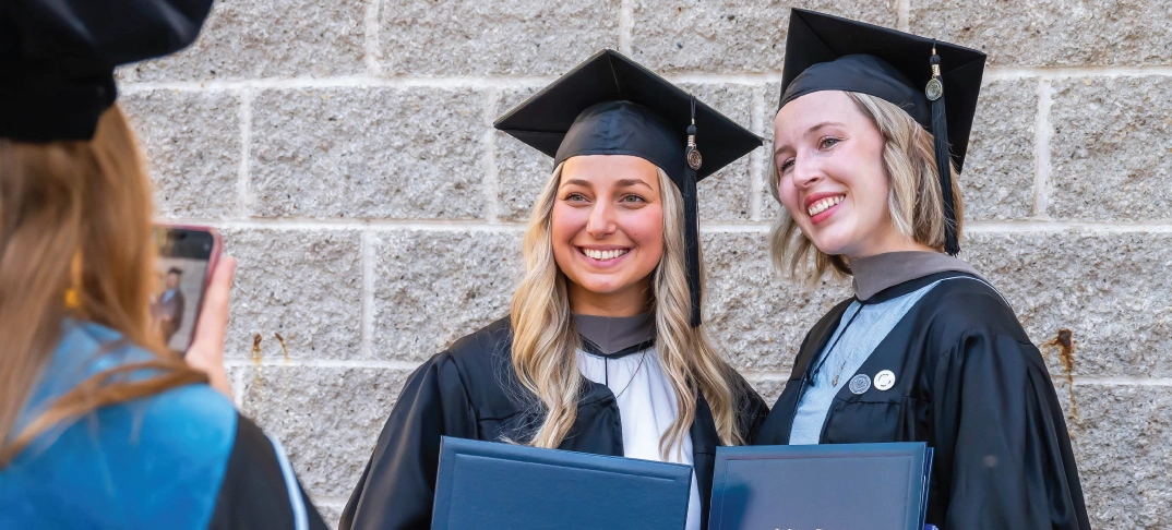 Two master degree graduates smiling and posing together outdoors.