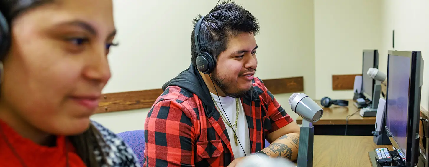 Two students wearing headphones observing a social work exercise with microphones and computers.