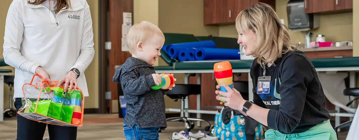 A woman conducting a pediatric assessment on the floor with a toddler.