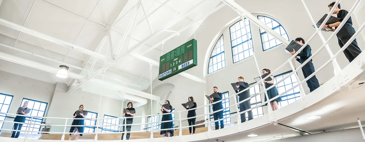 Several students standing around the Higgins balcony performing a song.