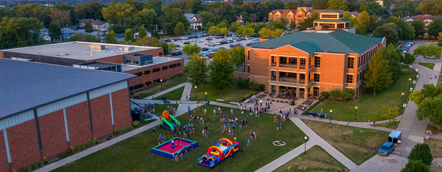 A large building surrounded by a spacious grassy area featuring bounch houses during a campus block party.