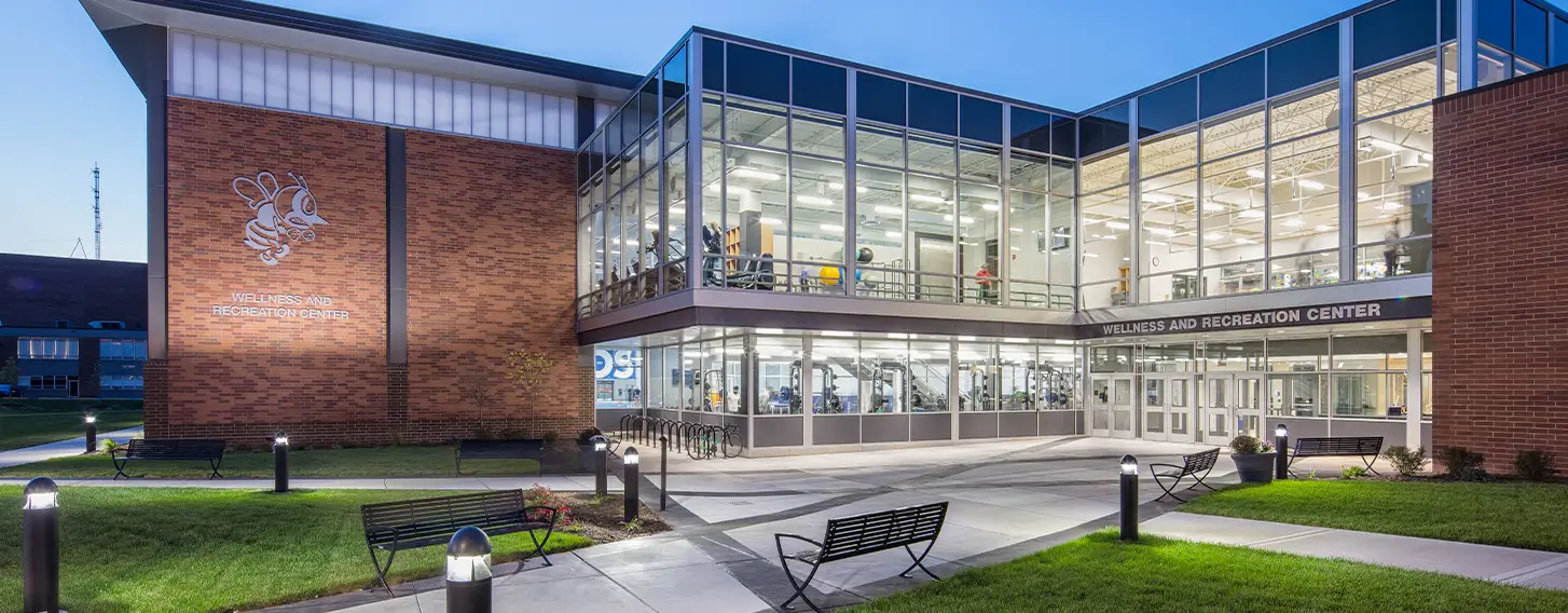 The St. Ambrose Wellness and Recreation Center at dusk featuring multiple people exercising inside.