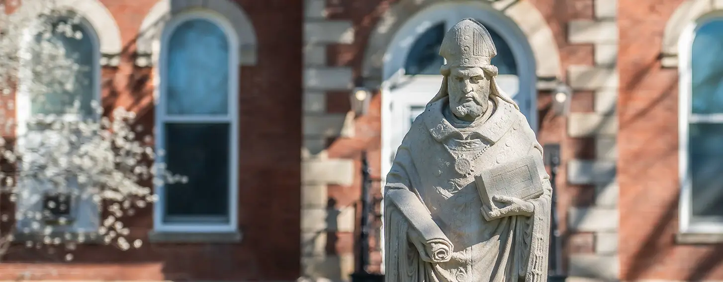 The statue of St. Ambrose in front of a brick building.