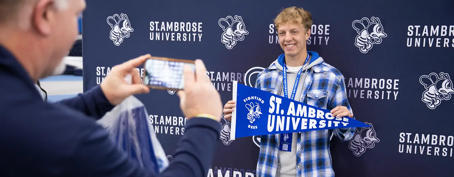 A student posing for a parent holding a St. Ambrose flag