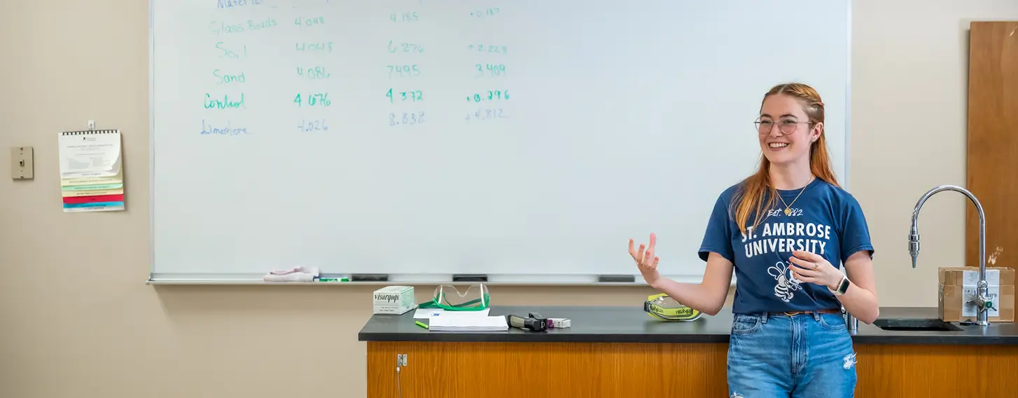 A student standing in front of a whiteboard in a classroom.