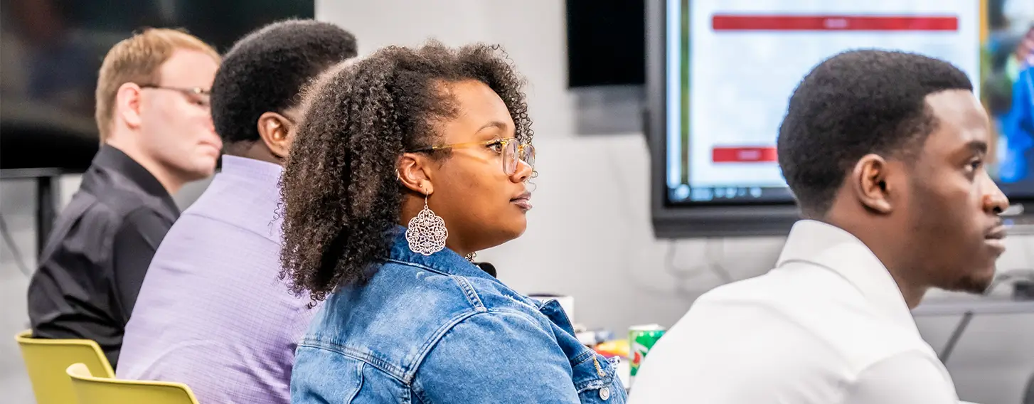 A woman sitting in a classroom alongside other students looking across the room.