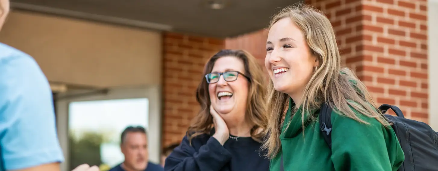 Student smiling with a parental figure outside