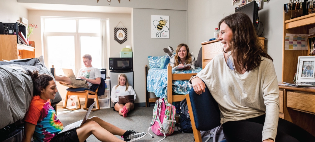 Group of students smiling and chatting in a dorm room.