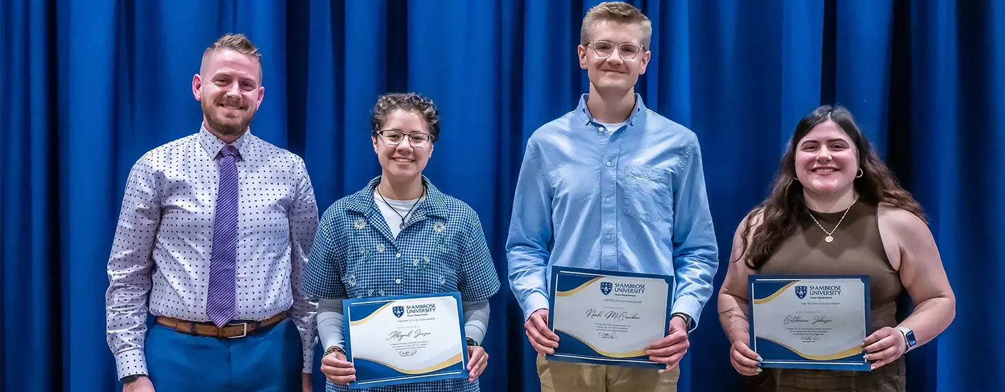 A group of students proudly displaying a scholarship certificate in front of blue curtains.