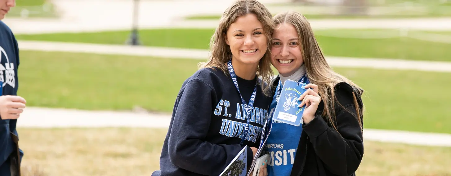 Two students posing together holding a name badge outside