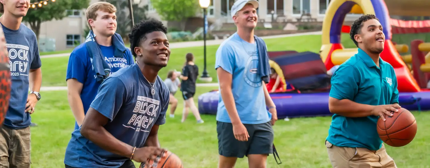 Two students shooting basketballs outside at an evening event