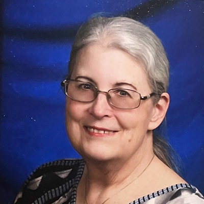 Becky Pracht smiles into the camera against a blue background.