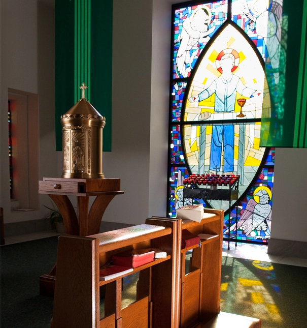 Sunlight shines through stained glass casting colorful light on kneelers and a tabernacle.