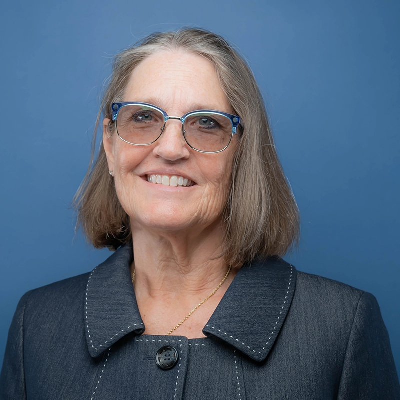 Lyn Ketelsen smiles into the camera against a blue background.