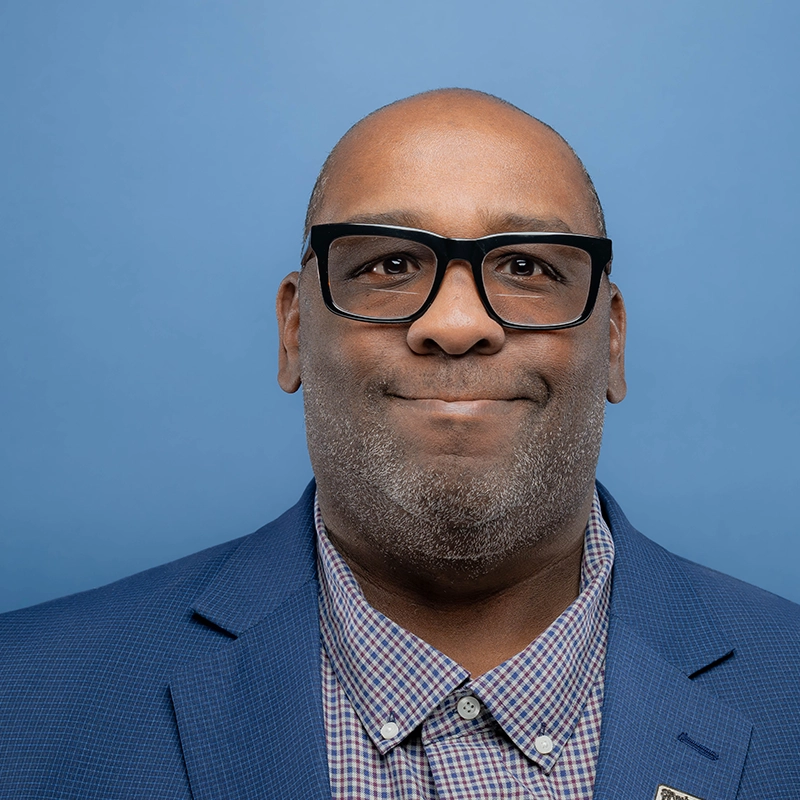 Mason Thomas IV smiles into the camera against a blue background.