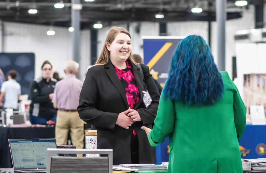 Student speaking with employer at career fair table, smiling.