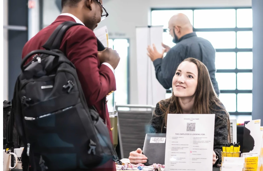 Woman sitting at table looks up at person during career fair.