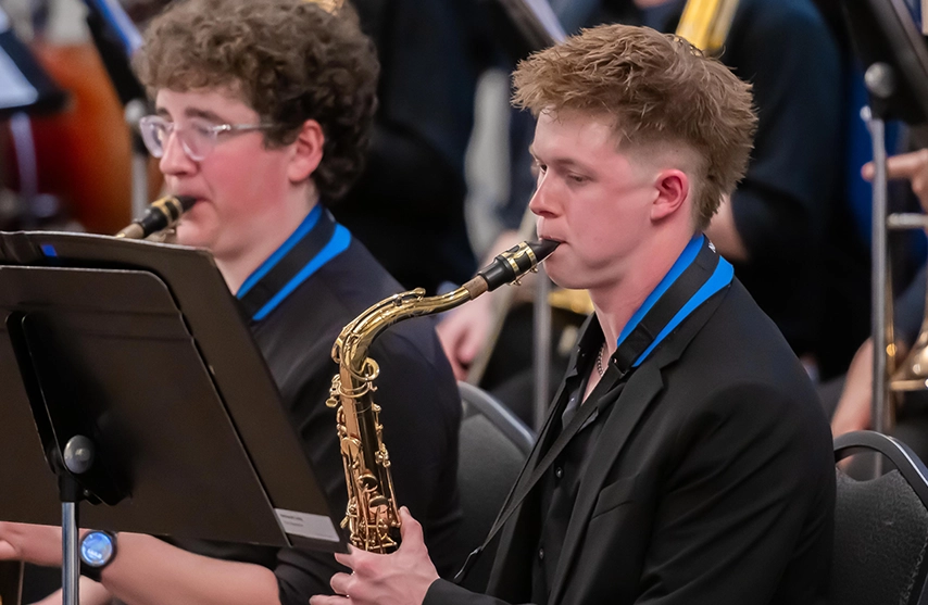 Two saxophonists perform, seated behind music stands during a concert performance.