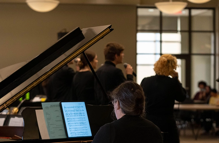 A pianist plays from sheet music in the foreground while SAU students sign into microphones in the background.