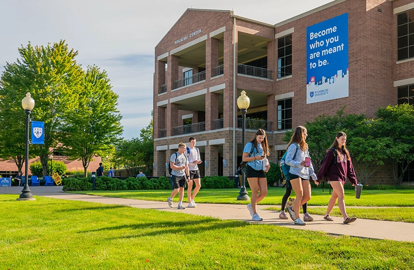 Students walk along a campus sidewalk in front of the Rogalski Center.