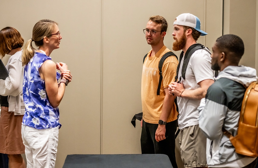 A woman stands and talks to a group of three students.