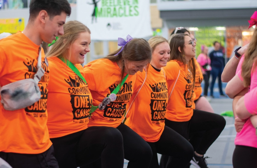 Students wearing orange shirts dancing in a line and smiling.