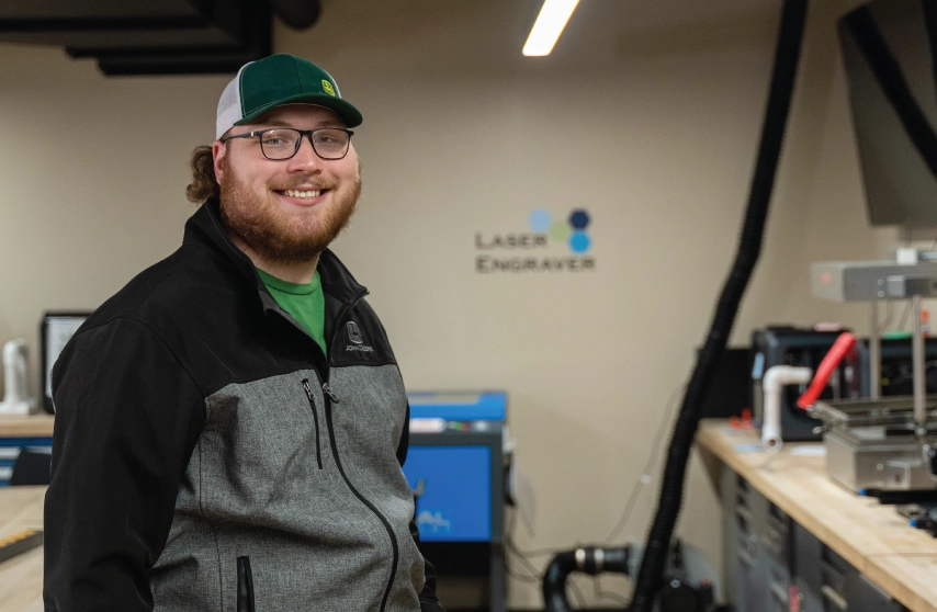 student standing in engineering lab in front of laser engraver.