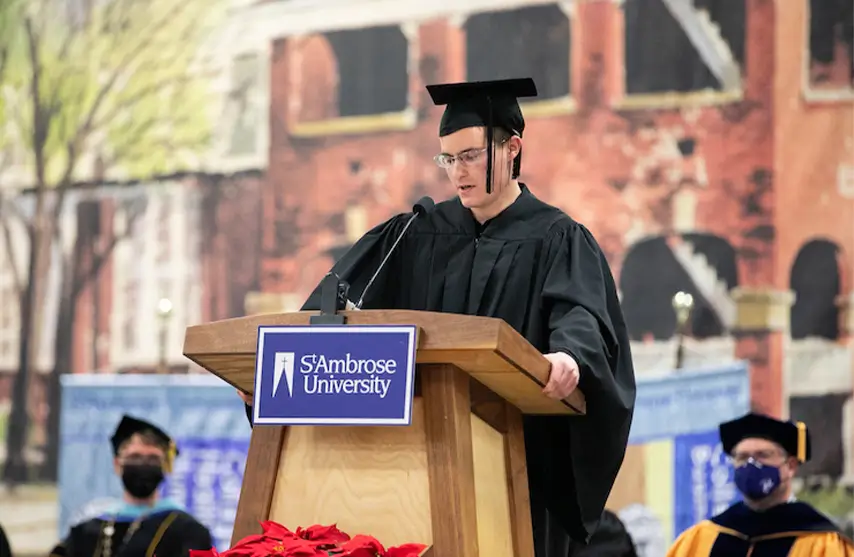 A man wearing a cap and gown speaking at commencement.