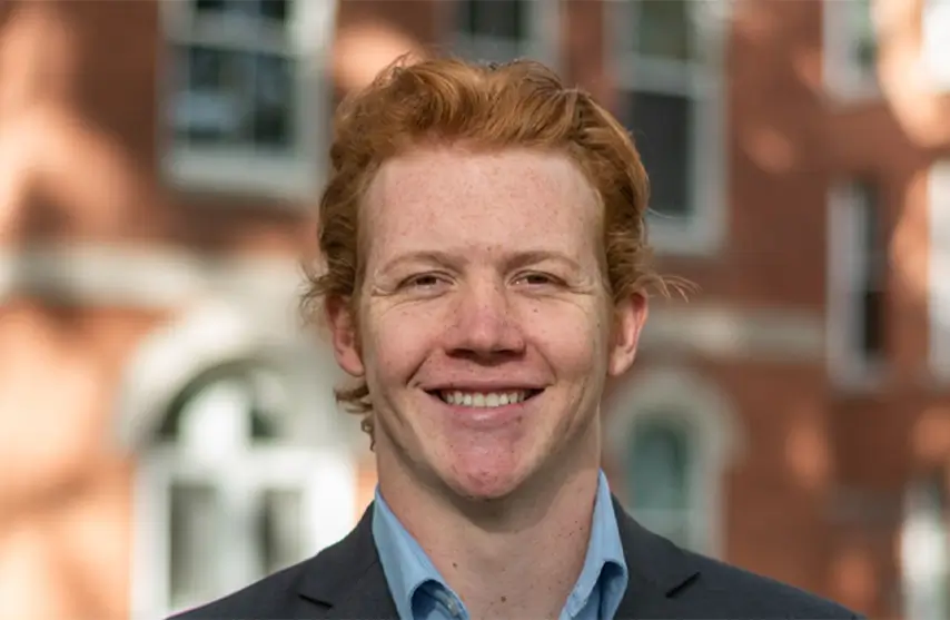 A male student smiling for a picture outside of Ambrose Hall.