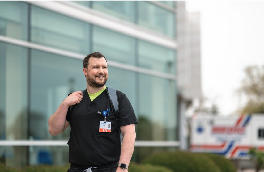 A man standing outside of a hospital wearing a nurses scrubs.