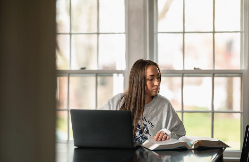 student at laptop, glancing aside at notes