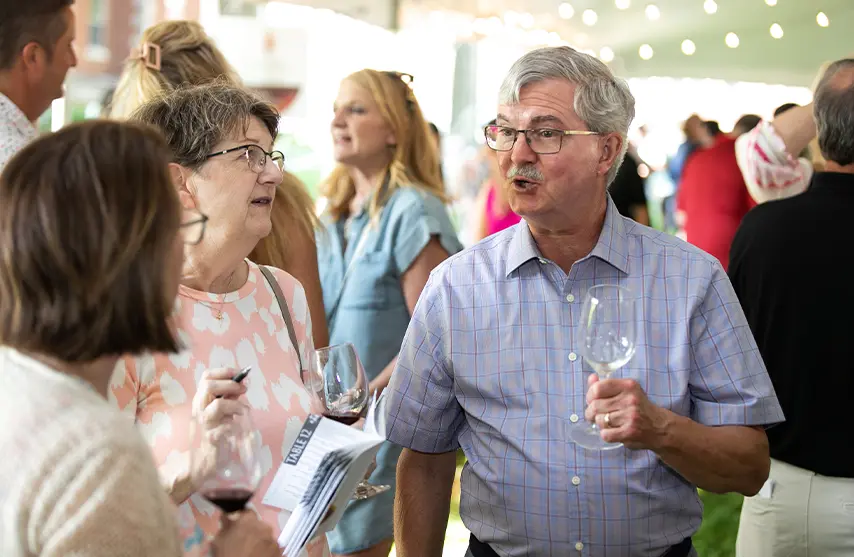 A group of people talk outside while holding wine glasses