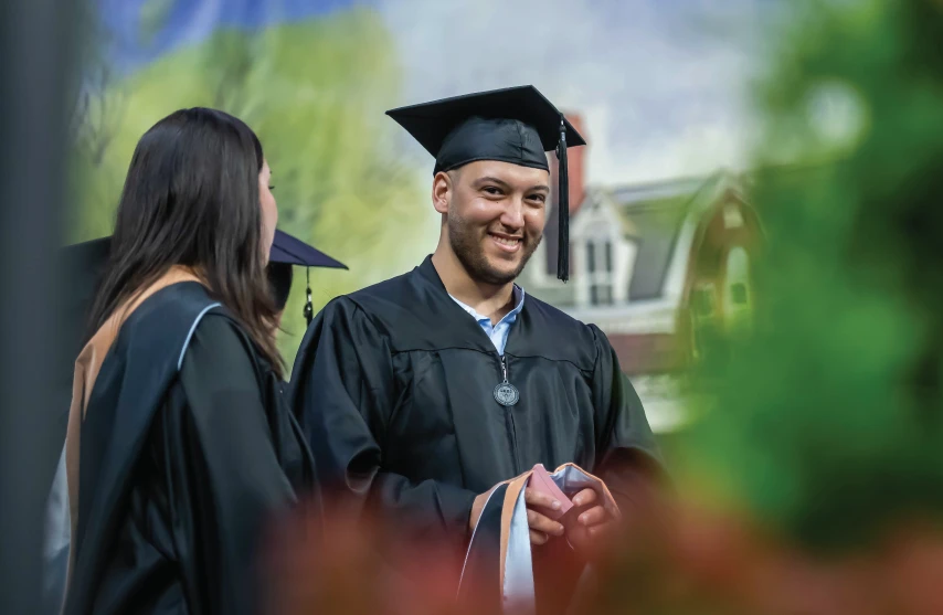 Graduate on stage smiling in cap and gown.