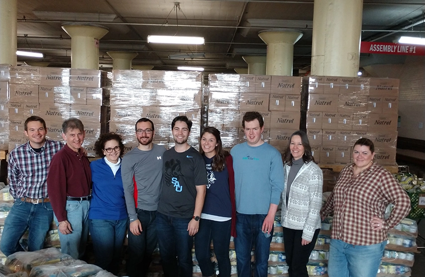 A group of volunteers stand in front of boxes of donated food.