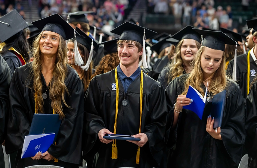 Three graduating seniors at St. Ambrose University's Commencement ceremony stand together.