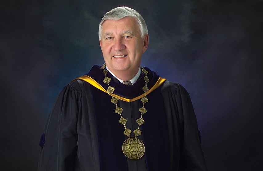 Dr. Edward Rogalski smiles into the camera while wearing the Presidential garb of St. Ambrose University.