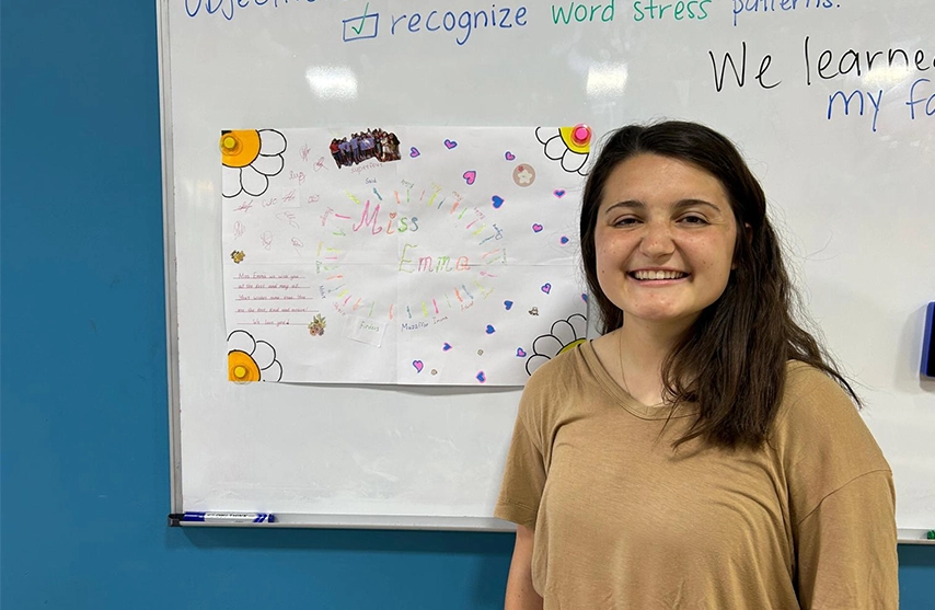 Emma Janecek stands in front of a colorful white board and smiles at the camera.