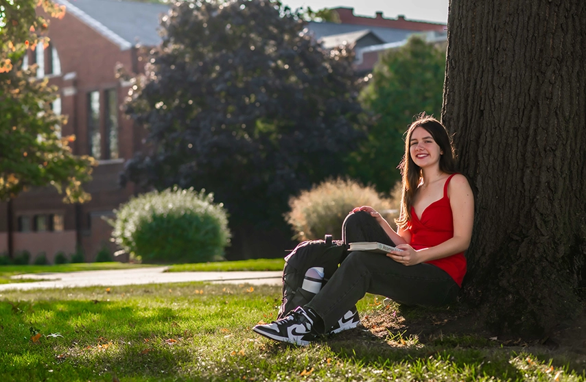 Katie Greer sits under a tree and smiles at the camera.