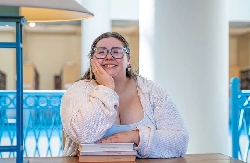 Nazaria Almanza-Gustafson, '26, smiles into the camera while sitting at a desk in the St. Ambrose University library.