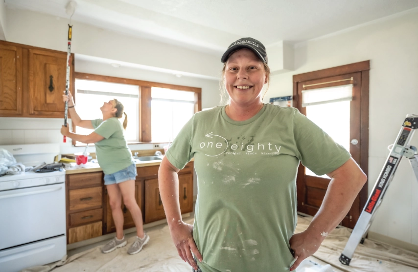 Two women smiling and painting a house.