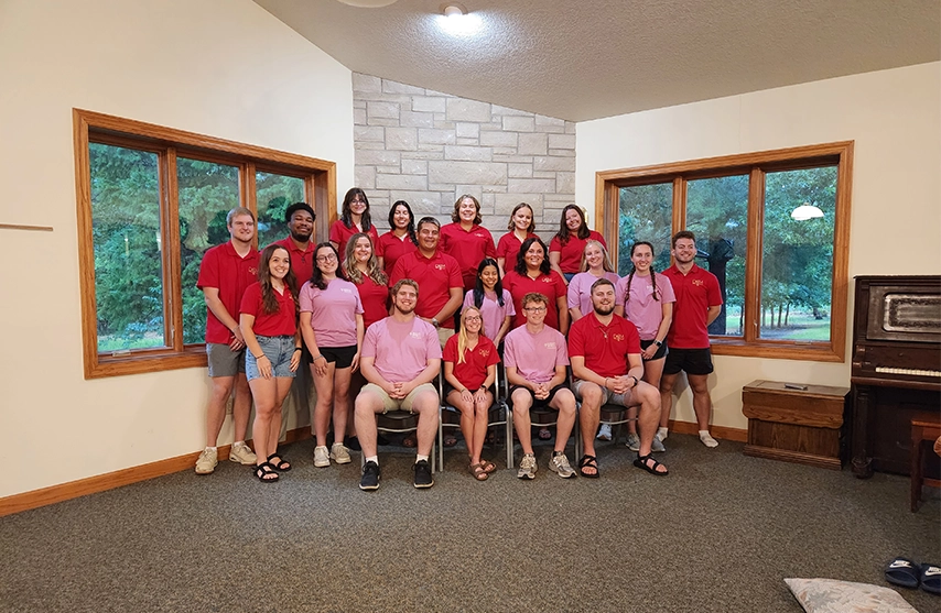 A group of Campus Ministry students from both St. Ambrose and Mount Mercy University campuses smile for a photo in front of a fireplace.