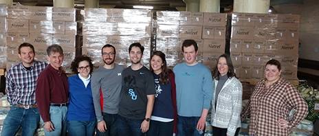 A group of volunteers stand in front of boxes of donated food.