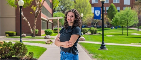 Delia Schwartz stands on St. Ambrose University's campus and smiles into the camera.