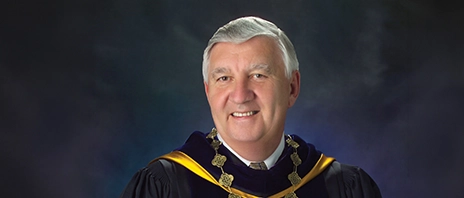 Dr. Edward Rogalski smiles into the camera while wearing the Presidential garb of St. Ambrose University.