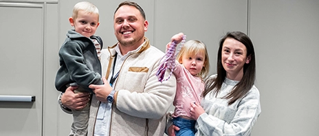 Kara DeBaker, her husband, and two kids smile at the camera.