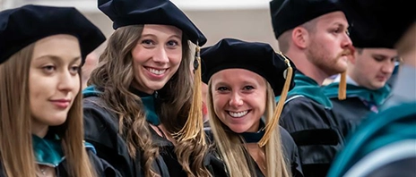 Two newly hooded physical therapy graduates smile at the camera.