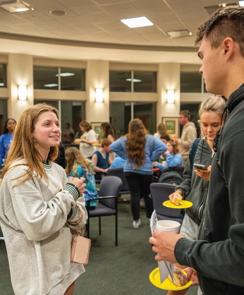 Two students talking indoors at Campus Ministry event.