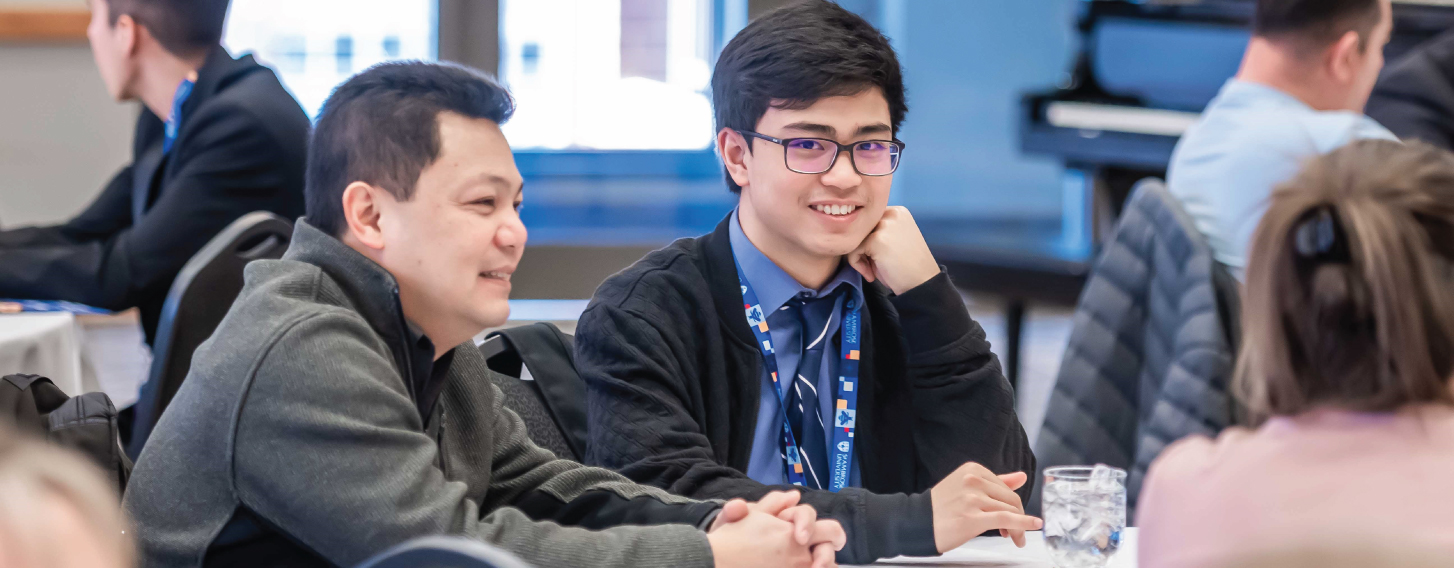 Male student in a tie sitting at a table with an adult