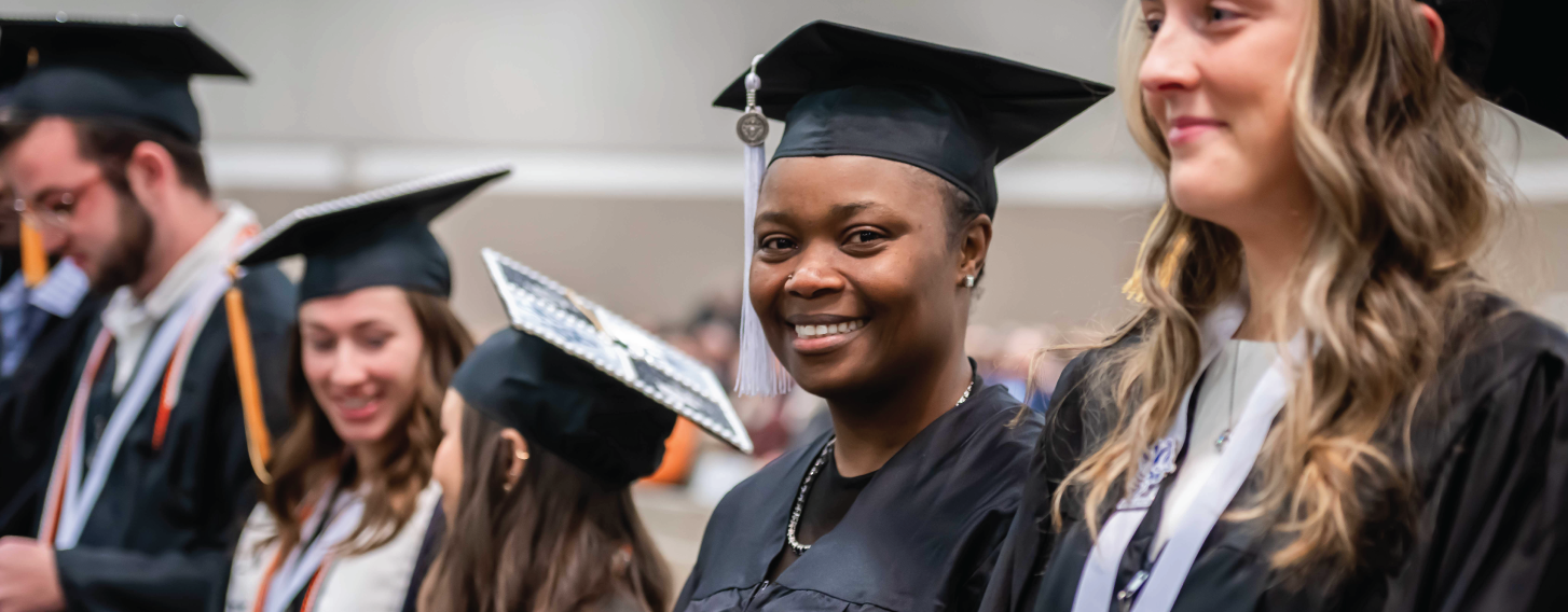 Student smiling at graduation in crowd.