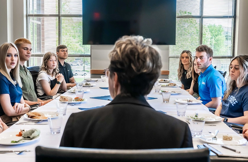 Amy Novak sits a table with student leaders. The plates on the table are filled with various amounts of food.